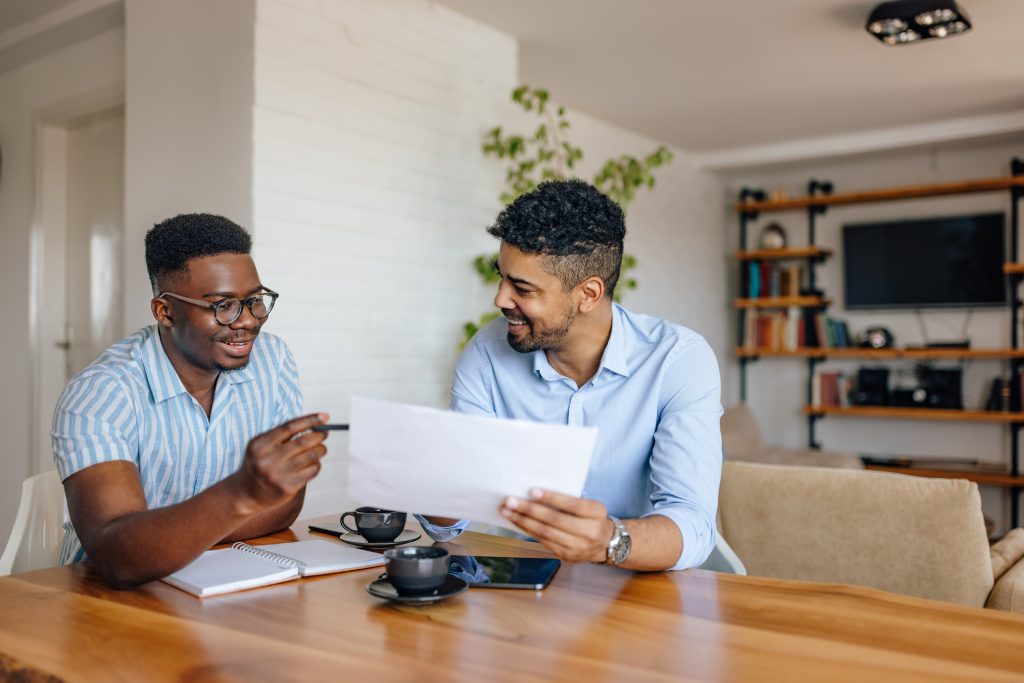 Two men discussing loan options, holding piece of paper, inside house.